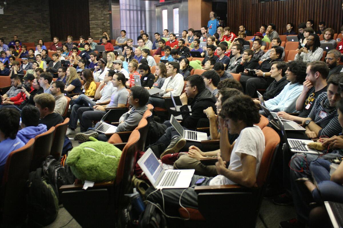 A full auditorium of people with laptops watching an opening presentation.